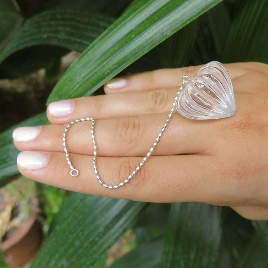 Lotus bud carved Crystal Clear Quartz crystal pendulum on hand with green leaves on the background