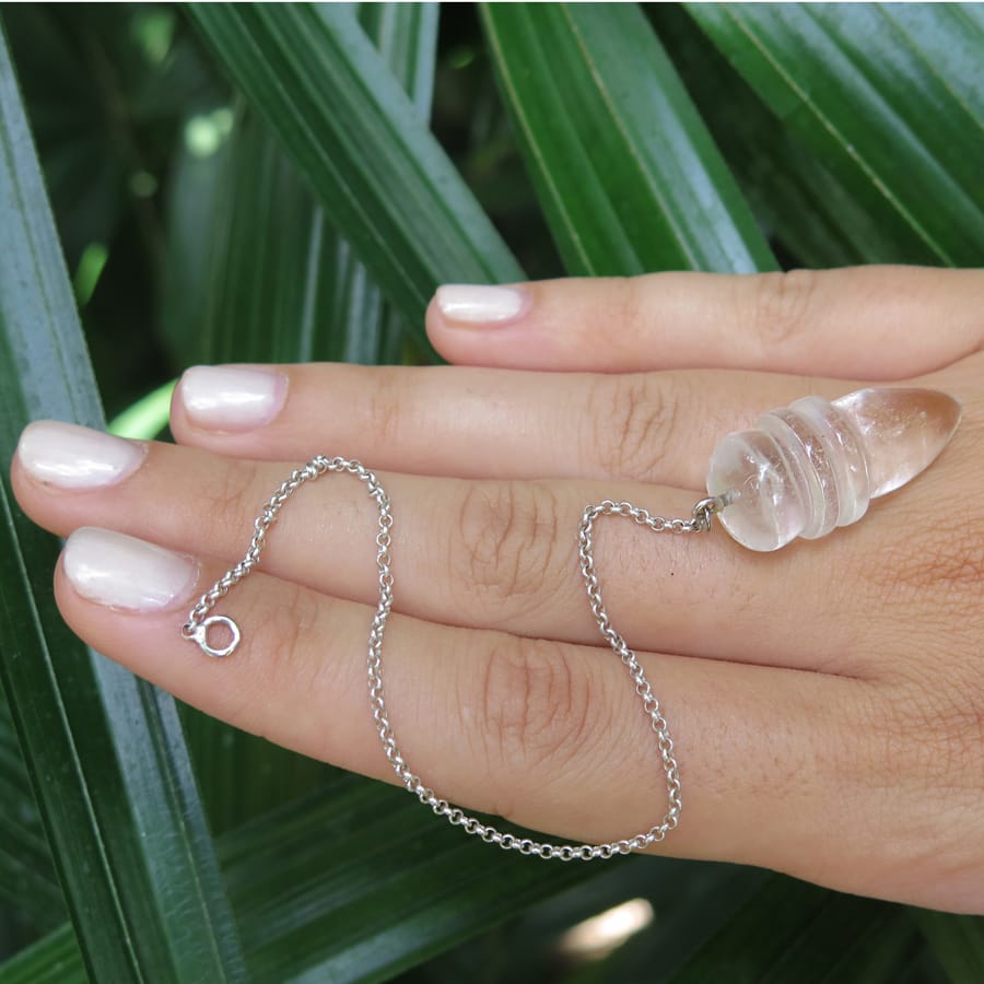 clear crystal pendulum point on hand with green leaves on the background