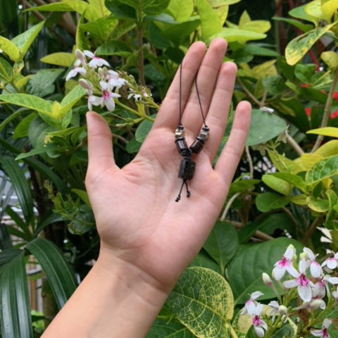 Talisman for protection with hematite, pyrite, and black tourmaline strung in an artificial black string on hand with green leaves on the background