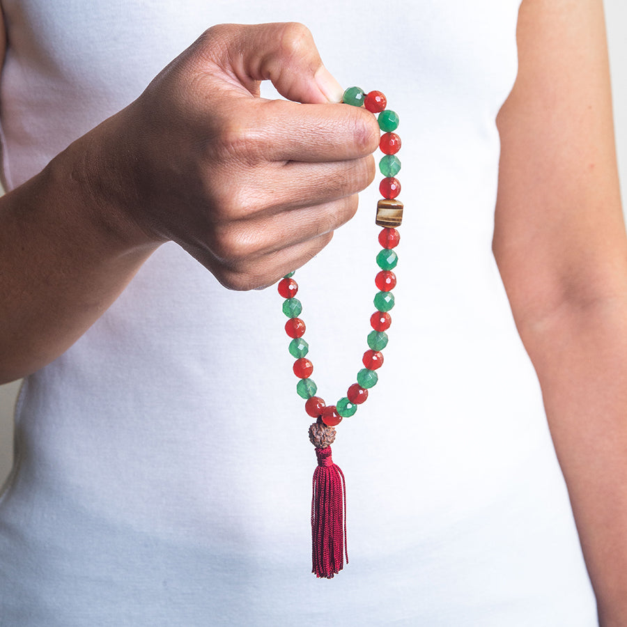 prayer beads tasbih with 33 beads of mixed Carnelian 8 mm and Aventurine 8 mm and Tiger’s Eye finished with Rudraksha seed and a dark red tassel on hand of a model in white top