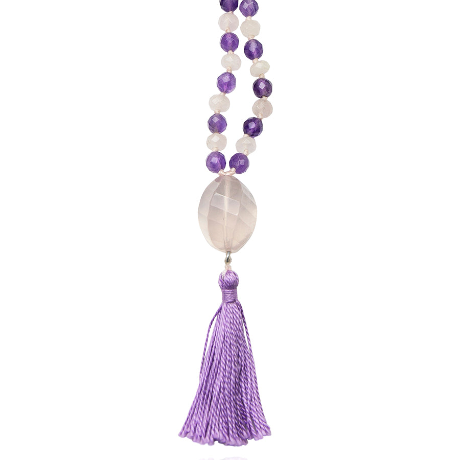 rose quartz pendant and purple tassel of a mala necklace on white background